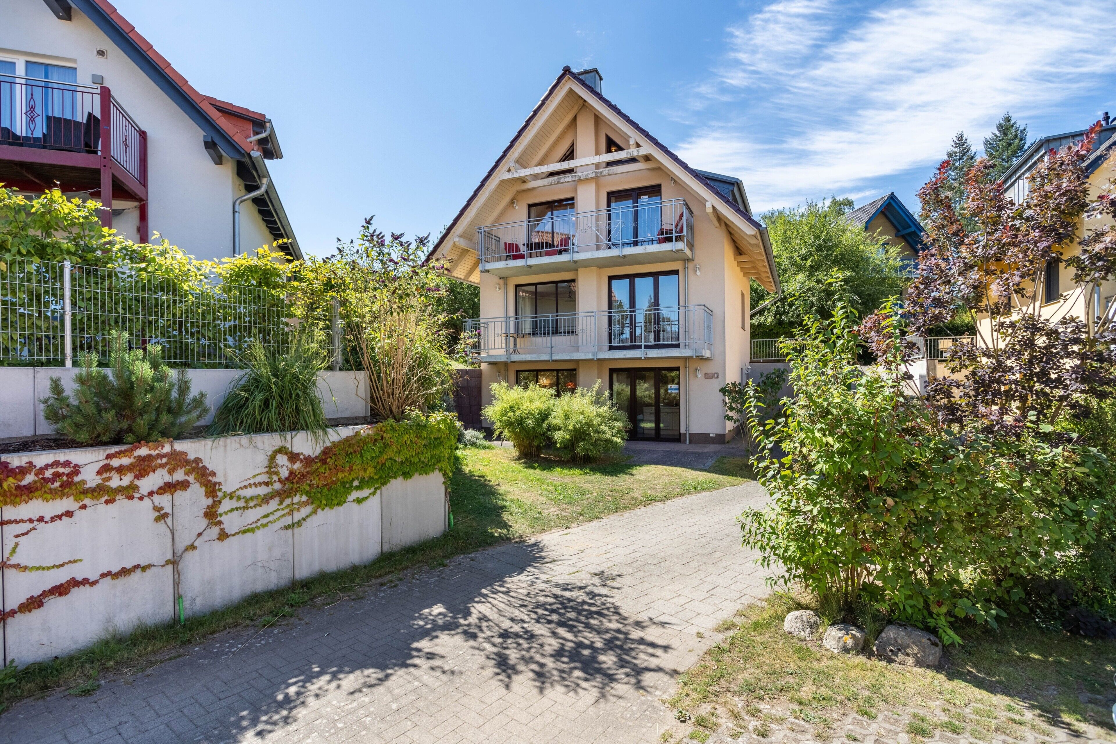 Un bâtiment à deux étages doté d’un balcon, d’un chemin pavé et entouré de verdure.