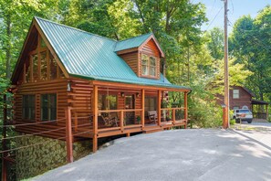 A log cabin with a green roof, a porch with chairs, and a stone foundation. - Log Cabin near Pigeon Forge | Hot Tub, Fireplace (Sevierville)