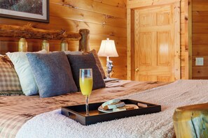 Een houten kamer met een bed, kussens, een dienblad met eten en drinken, en een lamp.