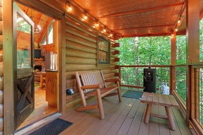 Een houten blokhut met een veranda, een bank, een tafel en een open haard.