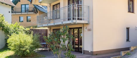 Un immeuble résidentiel à plusieurs étages, doté de balcons, d’une cour pavée et d’un petit jardin.