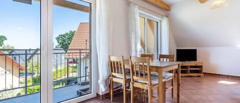 A spacious room with a dining table, chairs, a TV, and large windows.