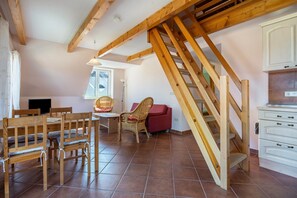 A room with a wooden staircase, a dining area with wooden furniture, and a kitchen with white cabinets. - Apartment '8 Og' with Private Garden and Balcony (Röbel)
