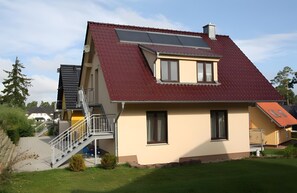 A house with a sloped roof, a balcony, and a staircase leading to the entrance. - Apartment '8 Og' with Private Garden and Balcony (Röbel)