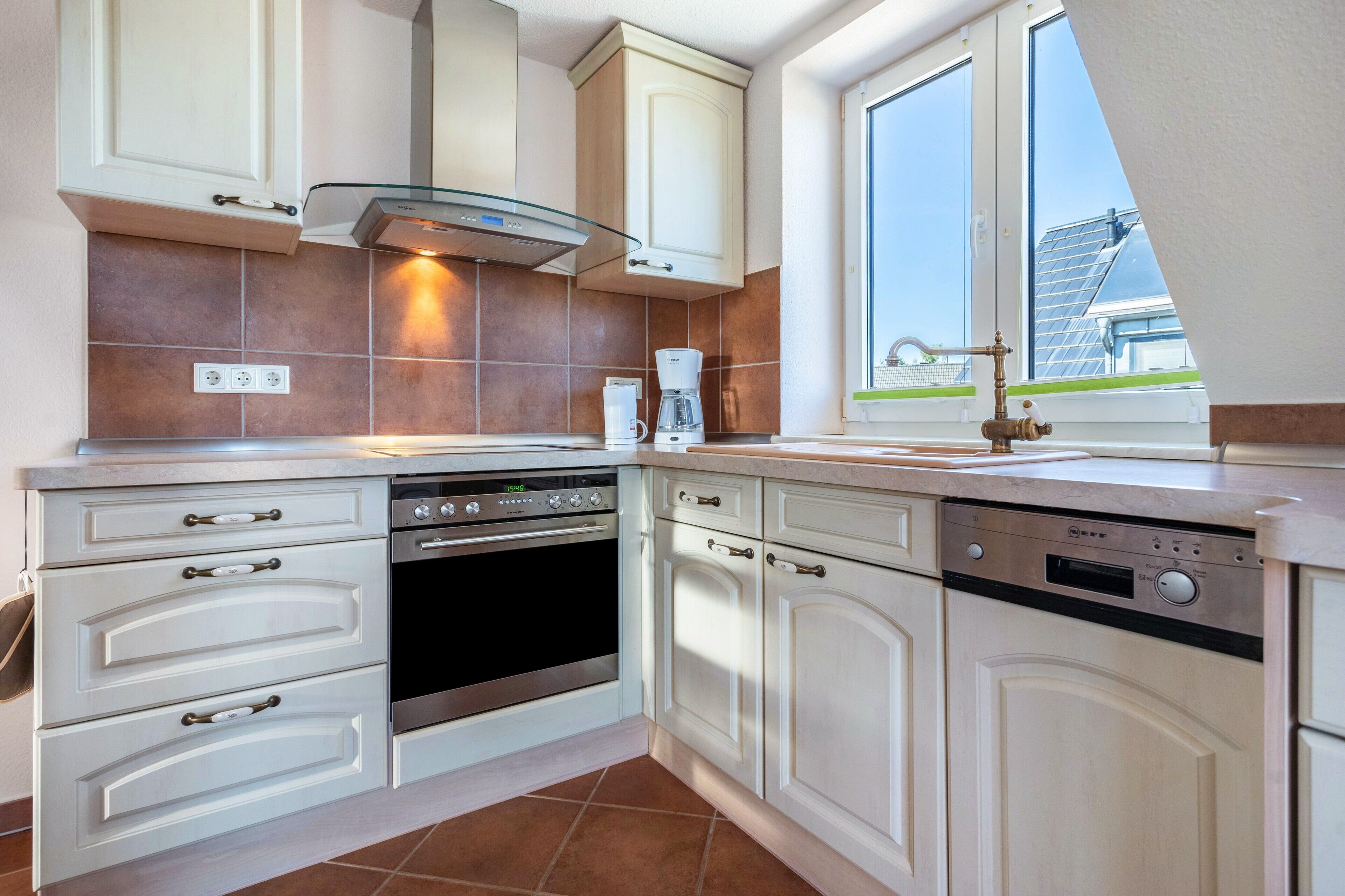 A kitchen with white cabinetry, a built-in oven, a dishwasher, and a coffee maker.