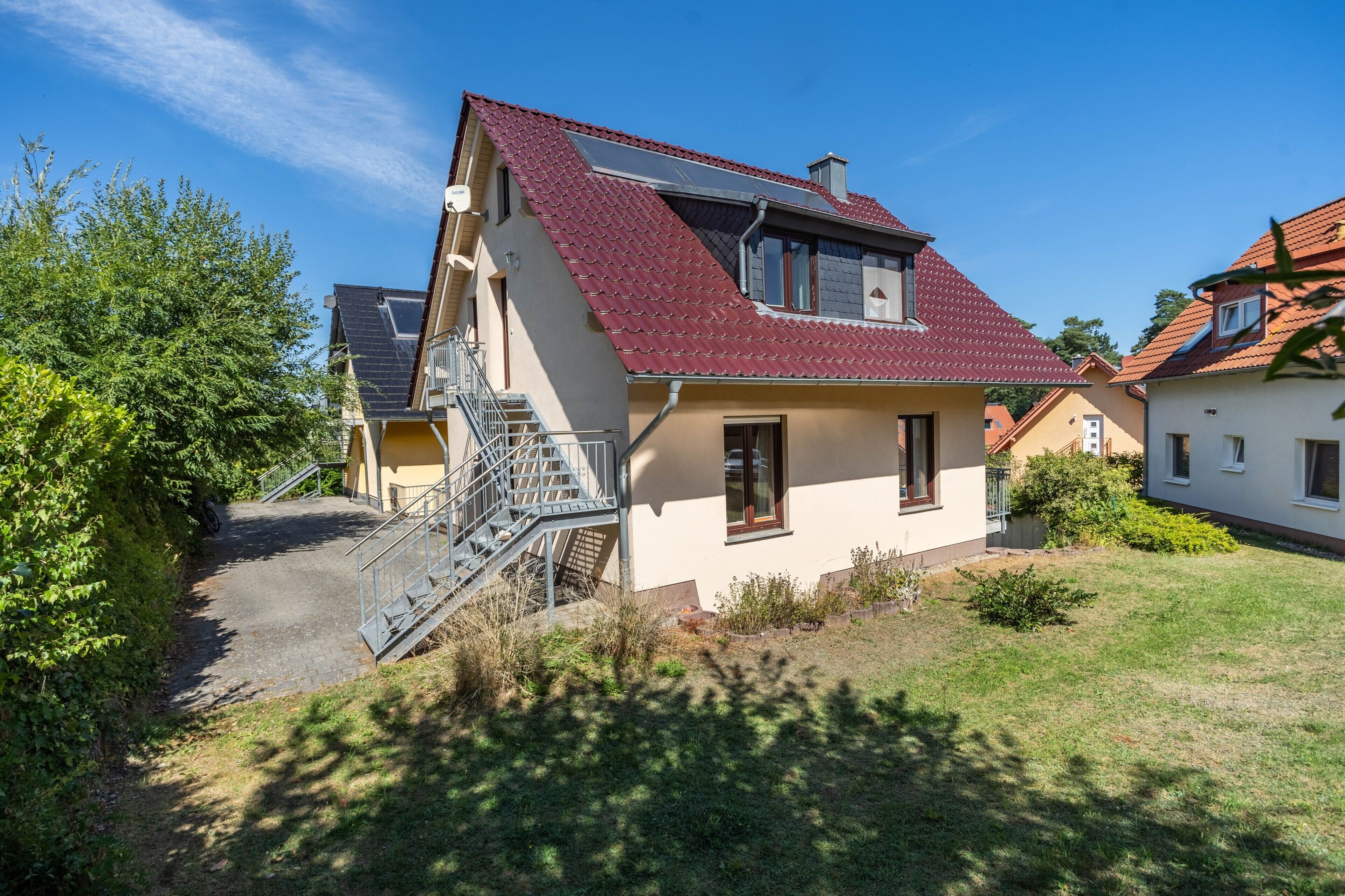 A two-story house with a red-tiled roof, a visible staircase, and a small garden area.