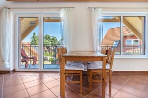 A dining area with a wooden table and chairs, a sliding glass door leading to a balcony with a view of a residential area. - Apartment '8 Og' with Private Garden and Balcony (Röbel)
