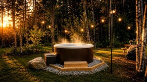Un bain à remous entouré d’une terrasse en bois, situé dans un espace boisé et illuminé de guirlandes lumineuses.
