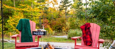 A fire pit with two red Adirondack chairs, a sign, and a mug.