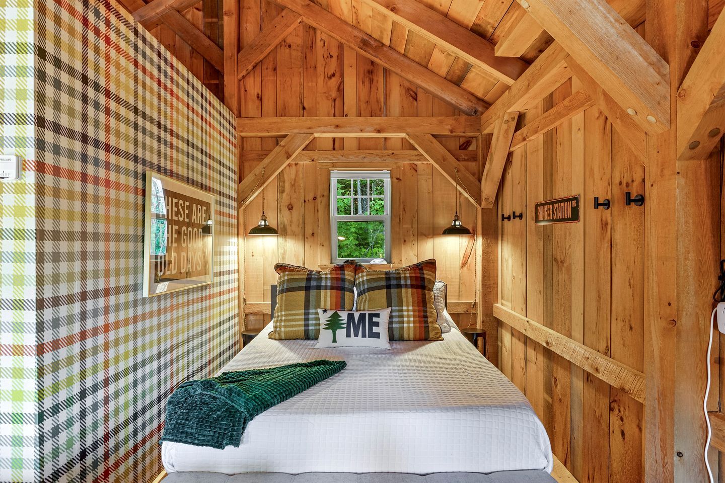 Une pièce chaleureuse en bois, avec un lit, des murs décorés d’un motif à carreaux, une fenêtre et une pancarte sur laquelle on peut lire : « À HESSE, LES JOURNÉES SONT BELLES ».