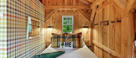 A cozy wooden room with a bed, plaid-patterned walls, a window, and a sign reading 'HESSE ARE GOOD DAYS.'