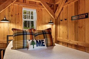 A cozy cabin room with a bed, plaid pillows, a window, and a sign reading 'RANGER STATION.' - Cozy Woodland Cabin Retreat – Peaceful Escape in Nature in Bethel, Maine (Bethel)