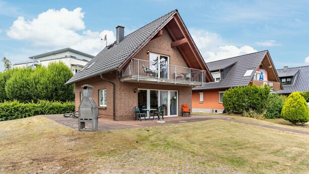 A two-story house with a balcony, a barbecue grill, and a paved driveway. - Apartment 'Haus 19 EG' with Private Terrace, Private Garden and Wi-Fi (Röbel)