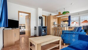 A modern living room with a sofa, a coffee table, a TV, and a kitchen area with a stove. - Apartment 'Haus 19 EG' with Private Terrace, Private Garden and Wi-Fi (Röbel)