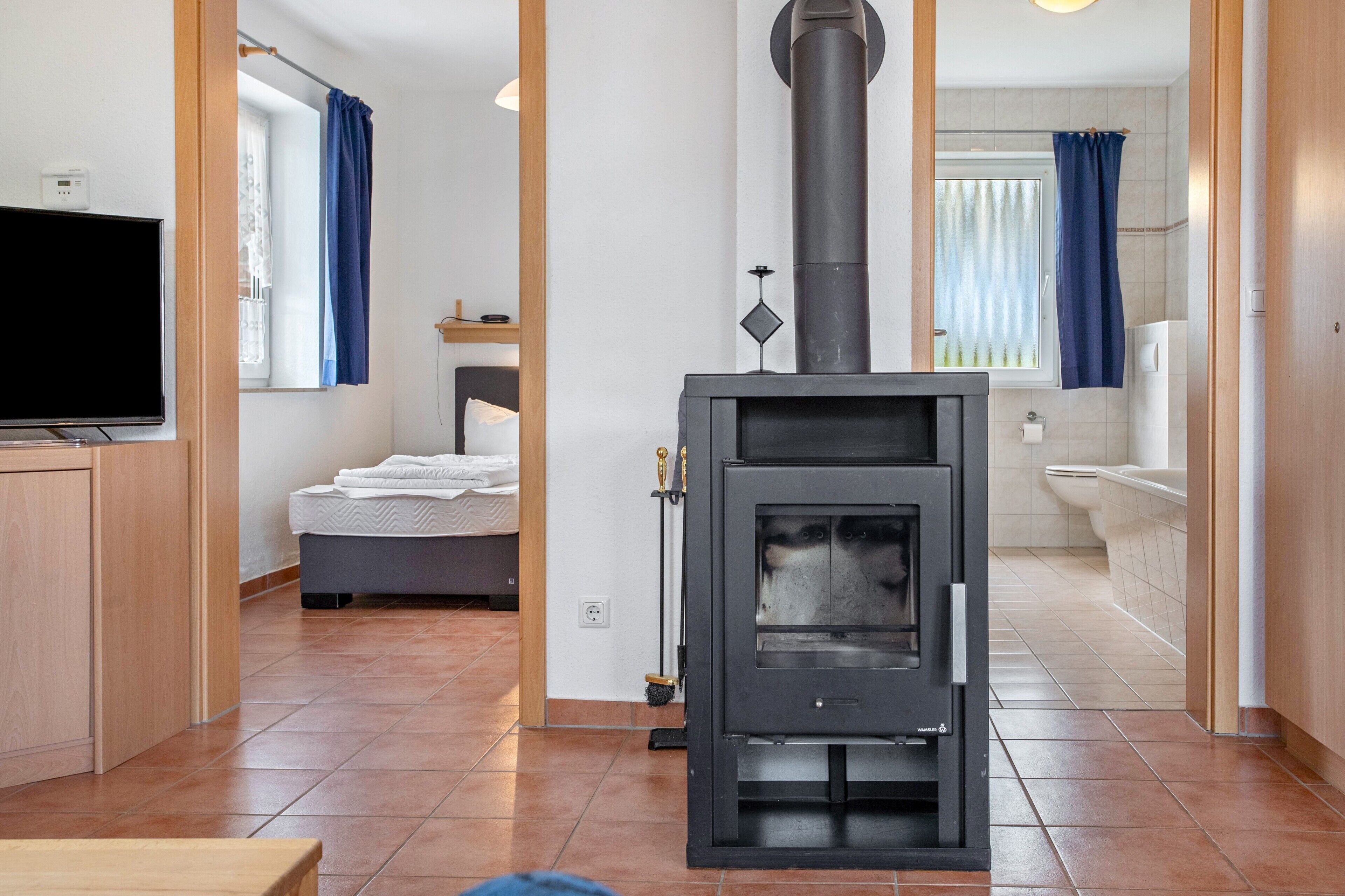 Ein zeitgemäßer Wohnraum mit Kaminofen, einem Bett, einem Fernseher und einem Badezimmer.