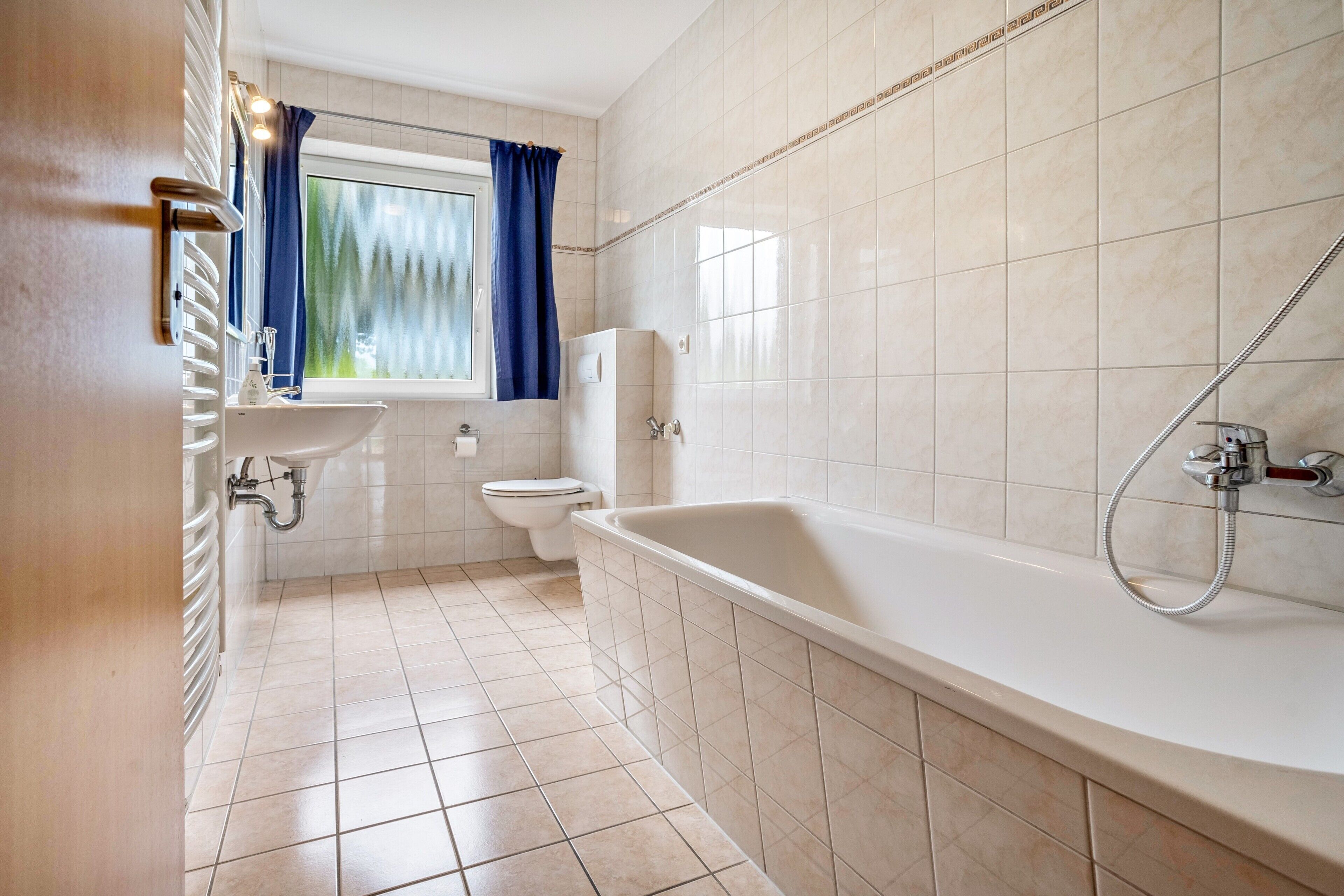 Ein Badezimmer mit Badewanne, Toilette, Waschbecken und einem Fenster mit Vorhängen.