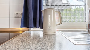 A kitchen with a white Siemens series 300 electric kettle on a granite countertop, a window with a view of a house, and a blue curtain. - Apartment 'Haus 19 EG' with Private Terrace, Private Garden and Wi-Fi (Röbel)