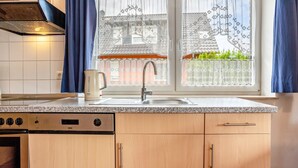A kitchen with a built-in oven, a sink, and a window with patterned curtains. - Apartment 'Haus 19 EG' with Private Terrace, Private Garden and Wi-Fi (Röbel)