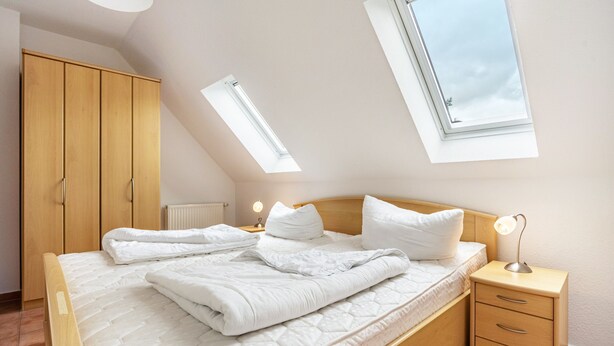 A bedroom with a bed, a nightstand, a wardrobe, and skylights. - Apartment 'Haus 19 OG' with Private Garden, Balcony and Wi-Fi (Röbel)