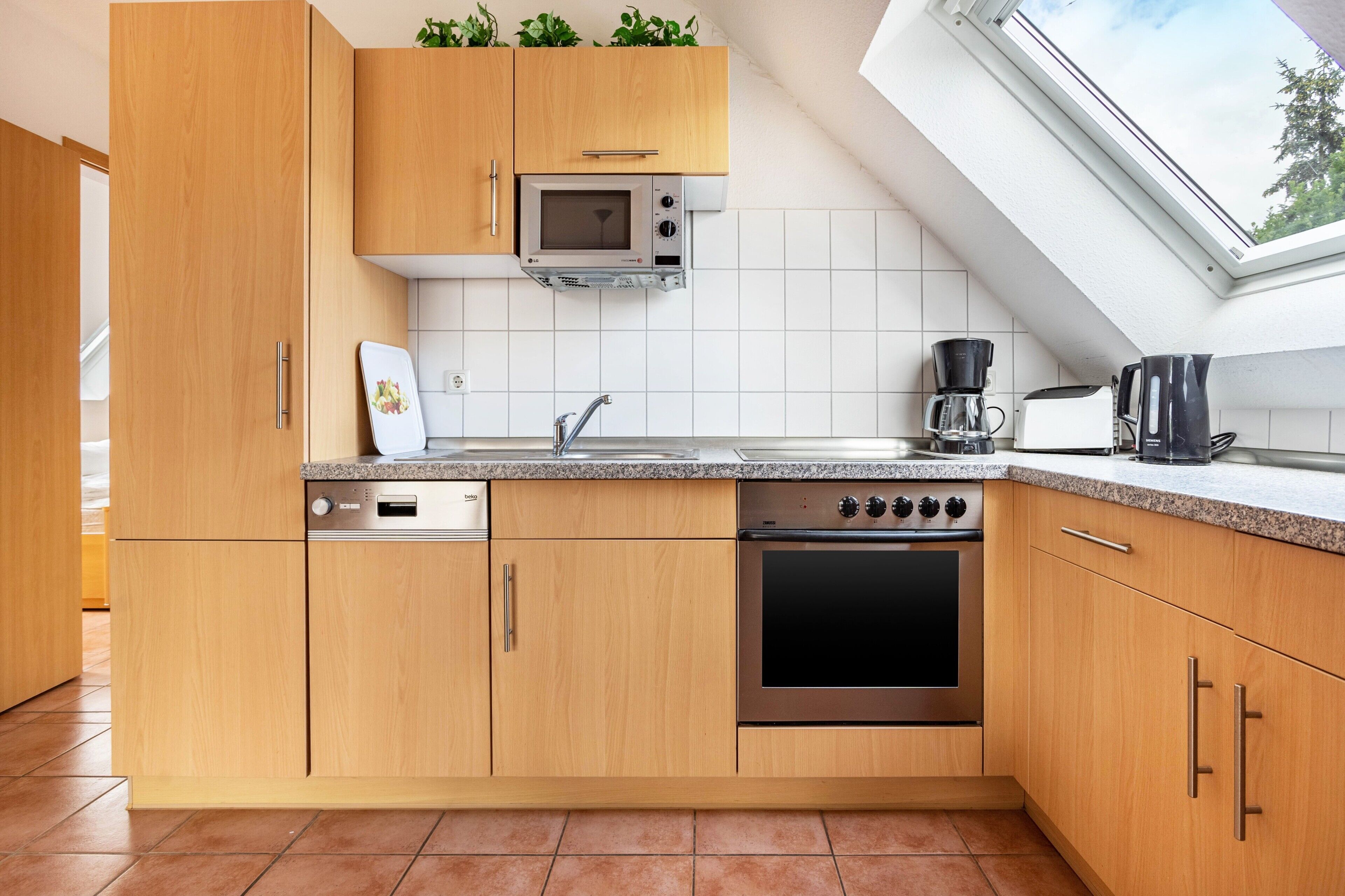 Eine moderne Küche mit Holzschränken, einer eingebauten Mikrowelle, einem Geschirrspüler, einem Backofen und einer Kaffeemaschine.