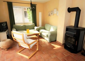 En stue med sofa, træstol, bord, fjernsyn, pejs og et vindue med gardiner.