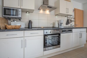 A modern kitchen with white cabinetry, a built-in oven, a coffee maker, and a microwave. - Holiday Home 'Haus K 95' with Private Terrace, Private Garden and Wi-Fi (Röbel)