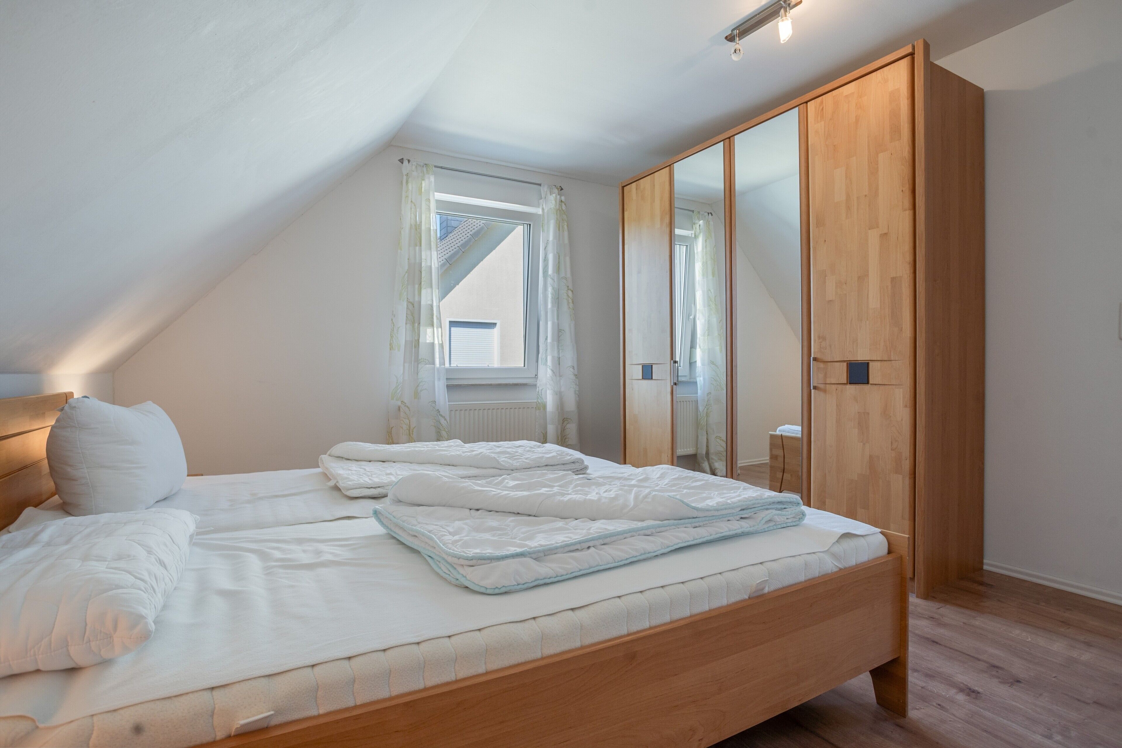 A bedroom with a wooden bed, a wardrobe, and a window with curtains.