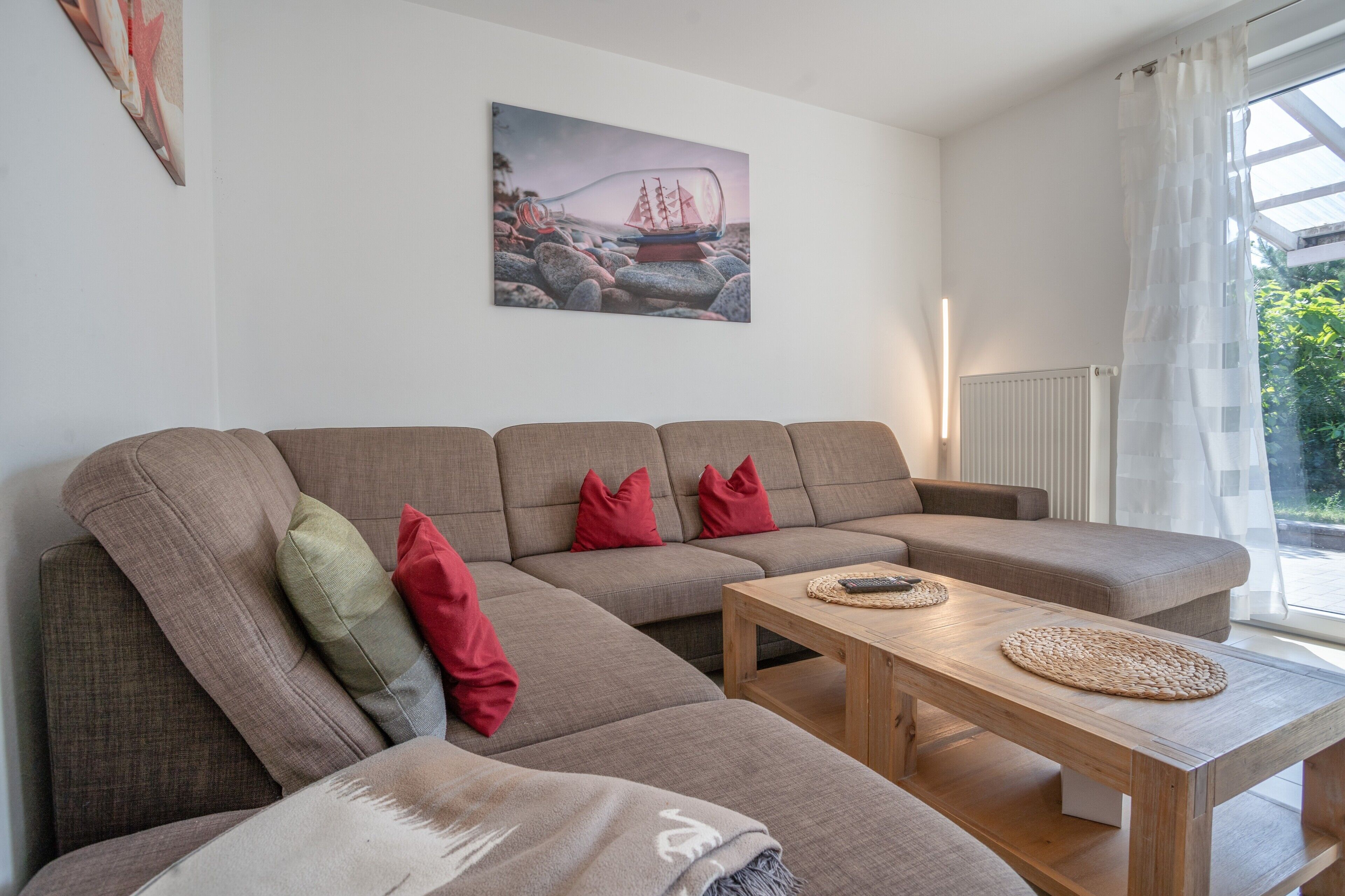 Un salon moderne avec un canapé d’angle, une table basse en bois et un tableau représentant un navire accroché au mur.