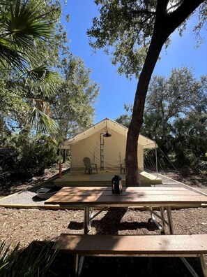 Un hébergement sous tente équipé d’une table de pique-nique, situé dans un cadre verdoyant.