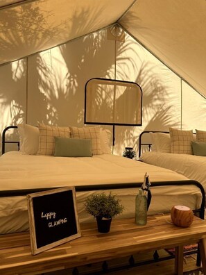 A tented room with a bed, a small table with a sign, and a potted plant. - Enjoyable Secluded Tented Cabin with Fire Pit in Sarasota, Florida (Sarasota)