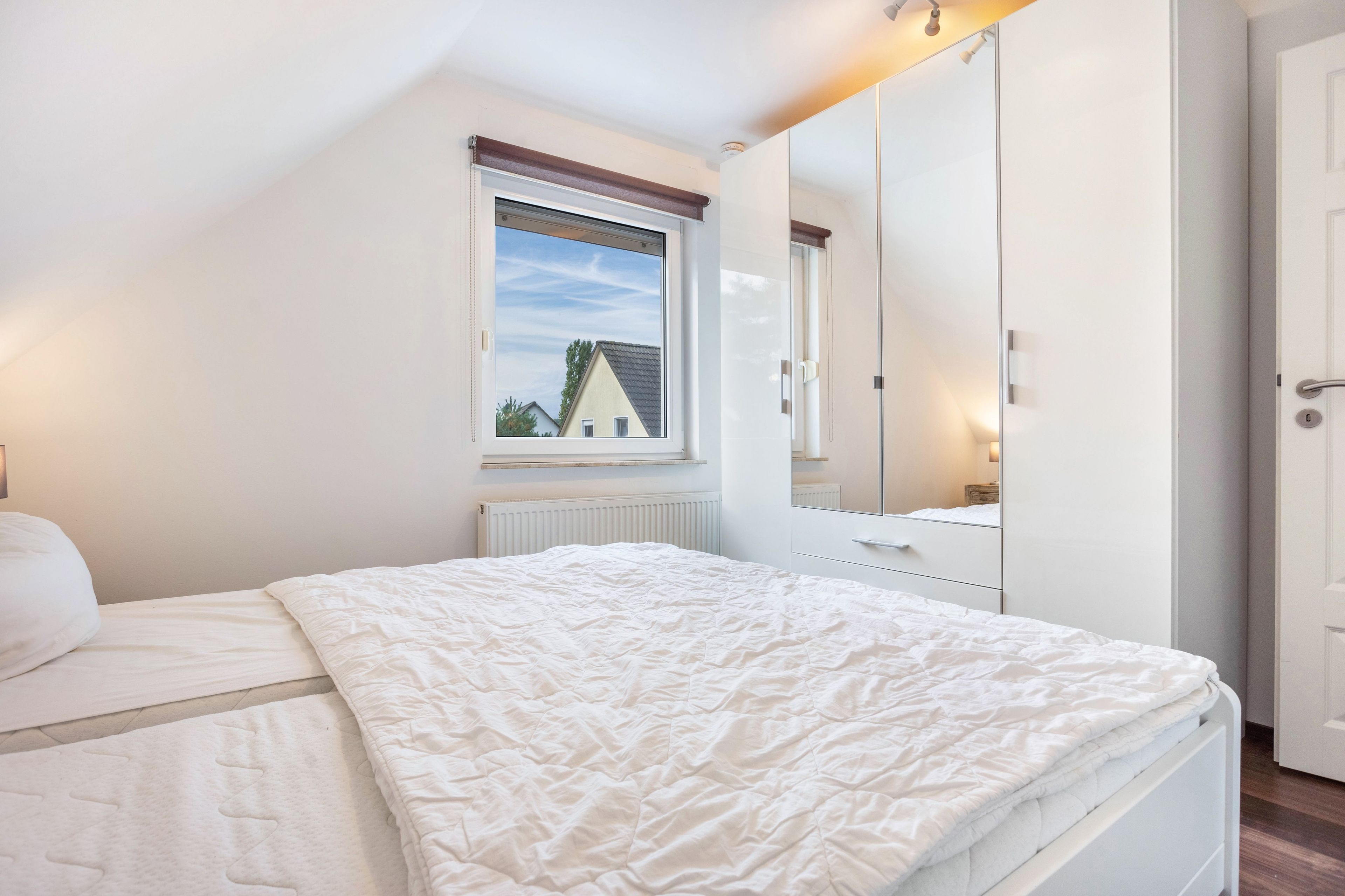 Ein Schlafzimmer mit Bett, Kleiderschrank, Fenster und Heizkörper.