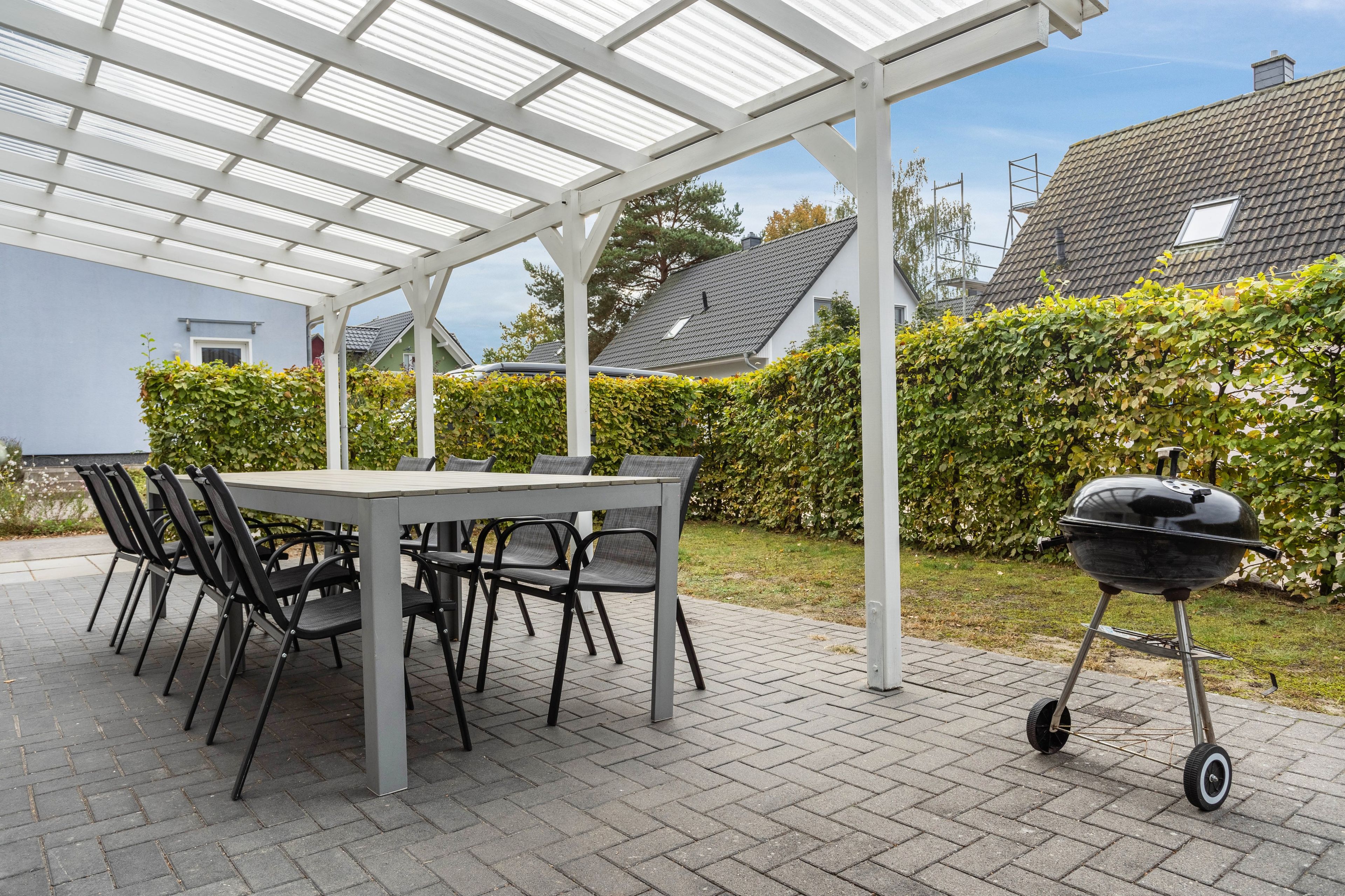Un patio exterior con una mesa y sillas, una parrilla y una zona cubierta con techo.