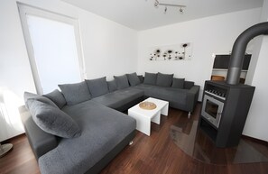 Ein modernes Wohnzimmer mit einem grauen Ecksofa, einem weißen Couchtisch, einem eingebauten Herd und einem Holzboden.