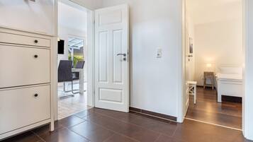Habitación de hotel con cama, mesita de noche y un pequeño taburete. Se ve una puerta que da a un balcón con mobiliario exterior.