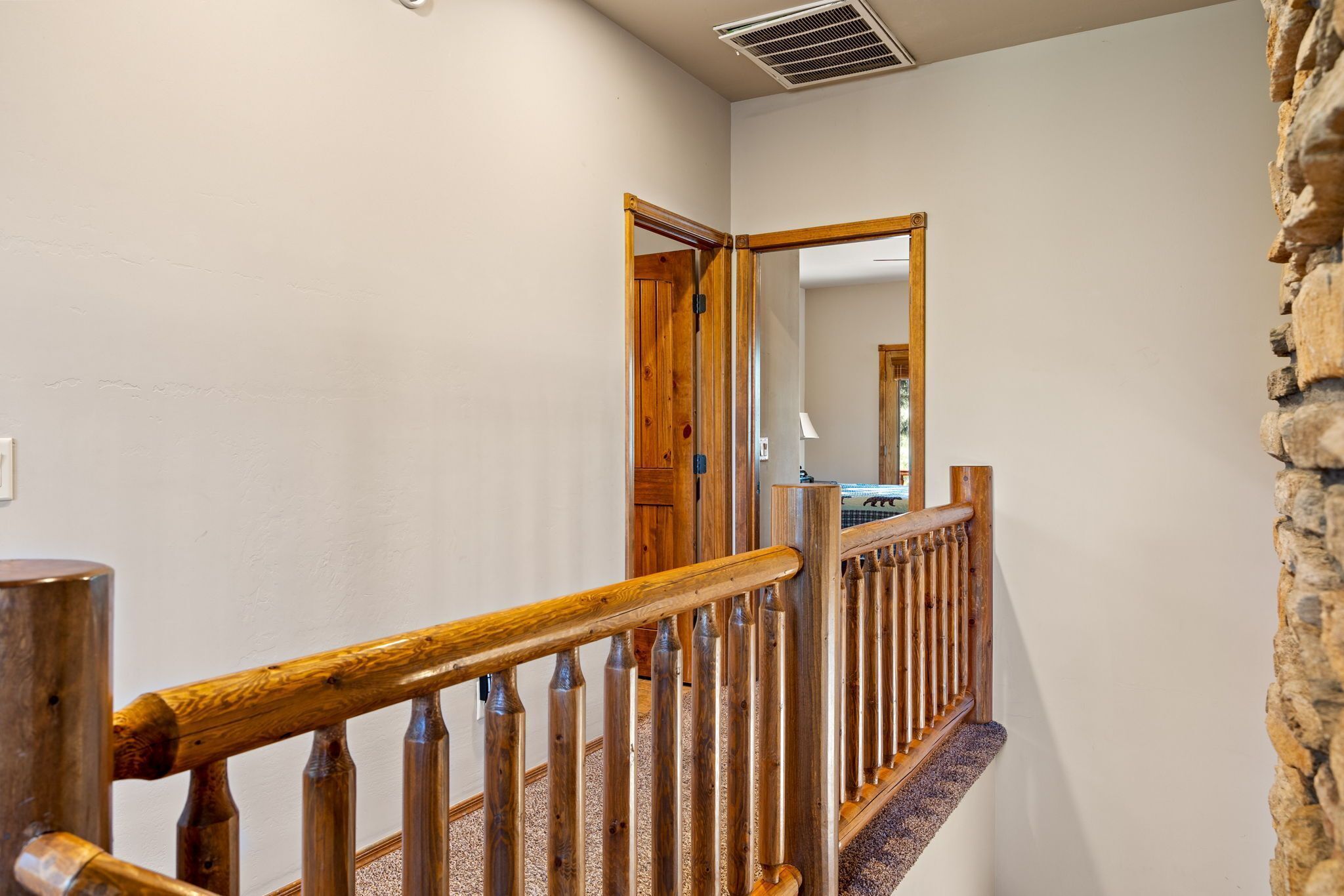 Un escalier en bois avec une rampe, des marches recouvertes de moquette et un mur en pierre d’un côté.