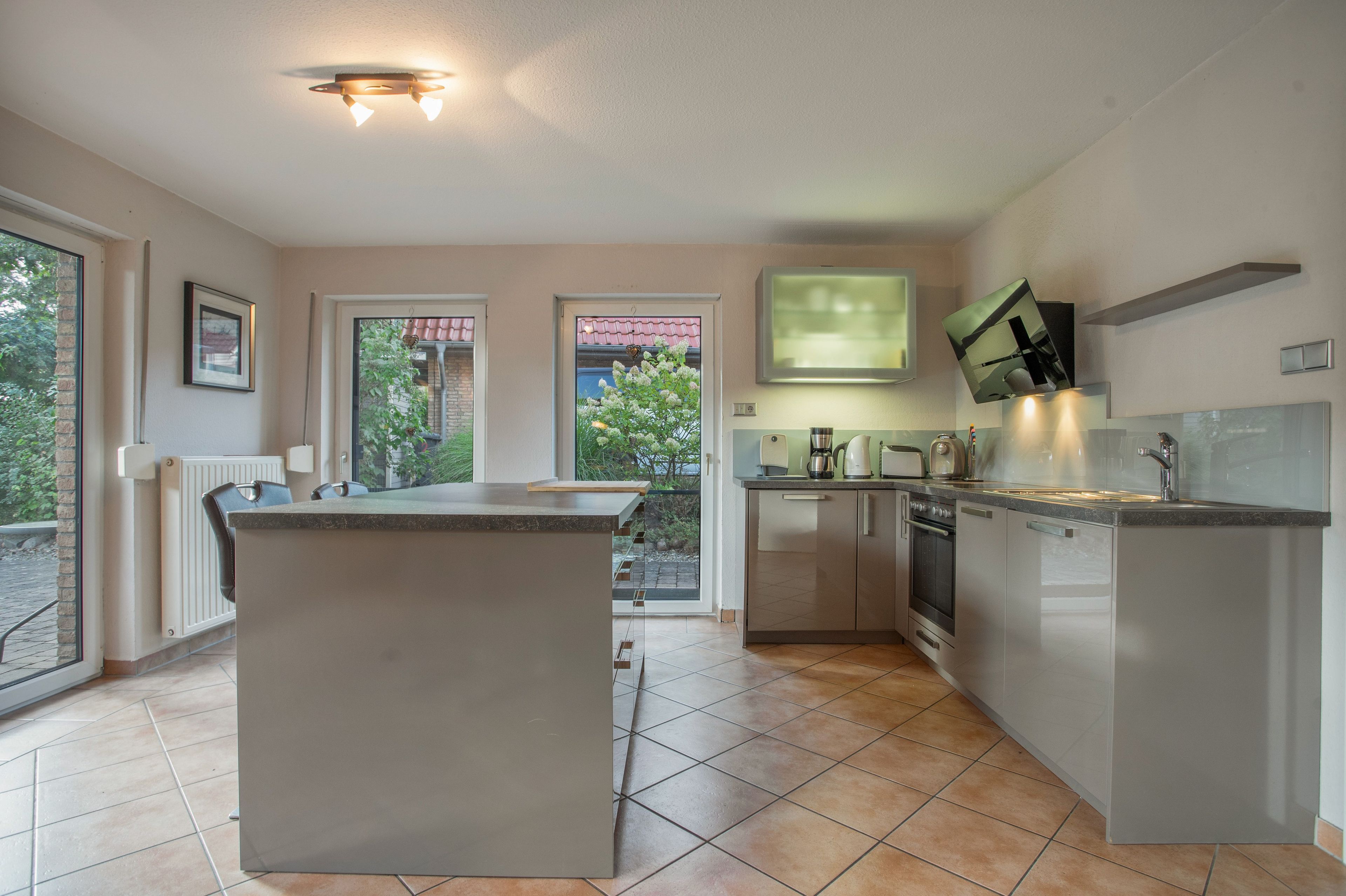 A modern kitchen with a central island, built-in oven, and a large window providing a view of the outdoors.