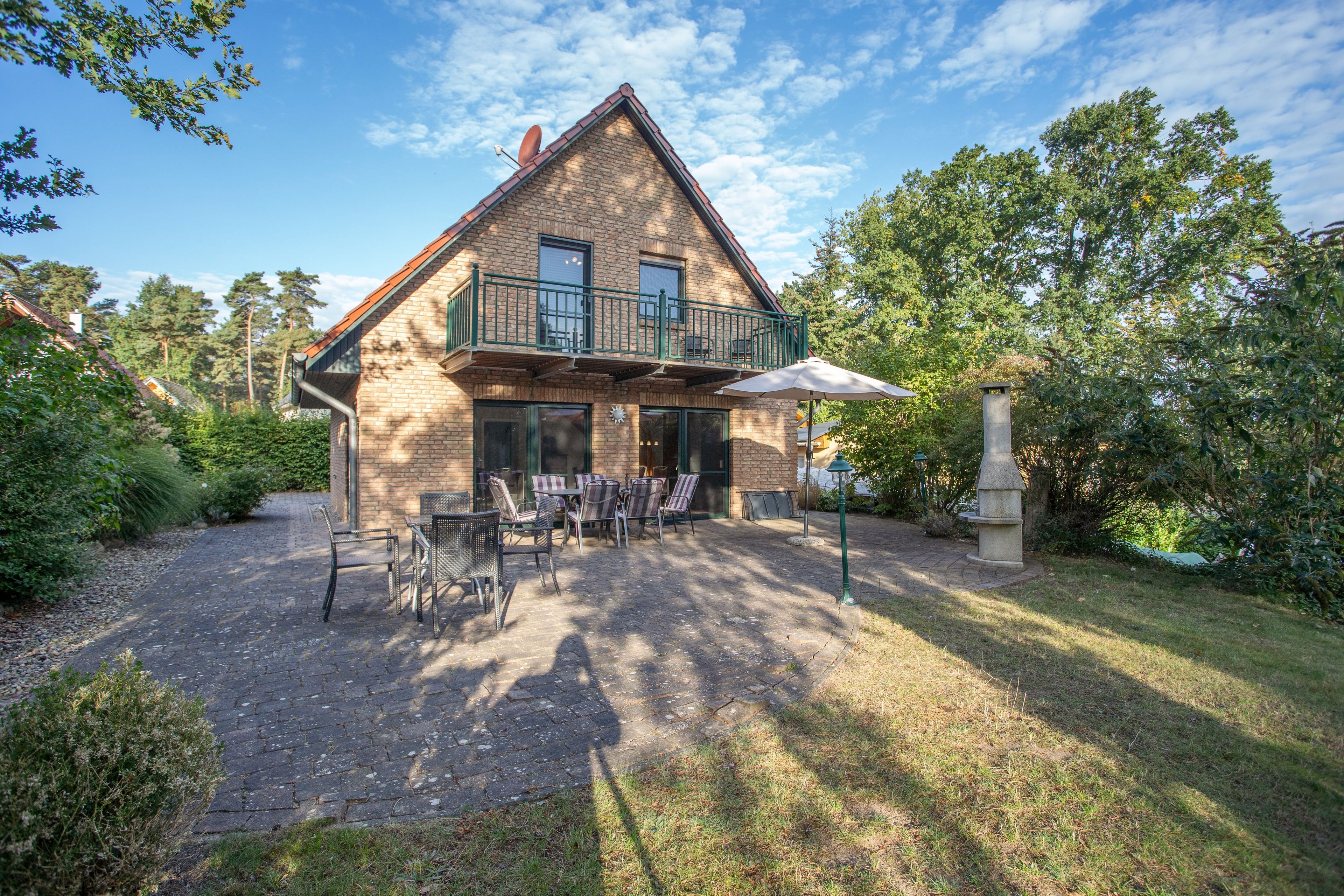 Une maison à deux étages avec un balcon, un espace extérieur aménagé avec des chaises et des tables, et une terrasse dallée.