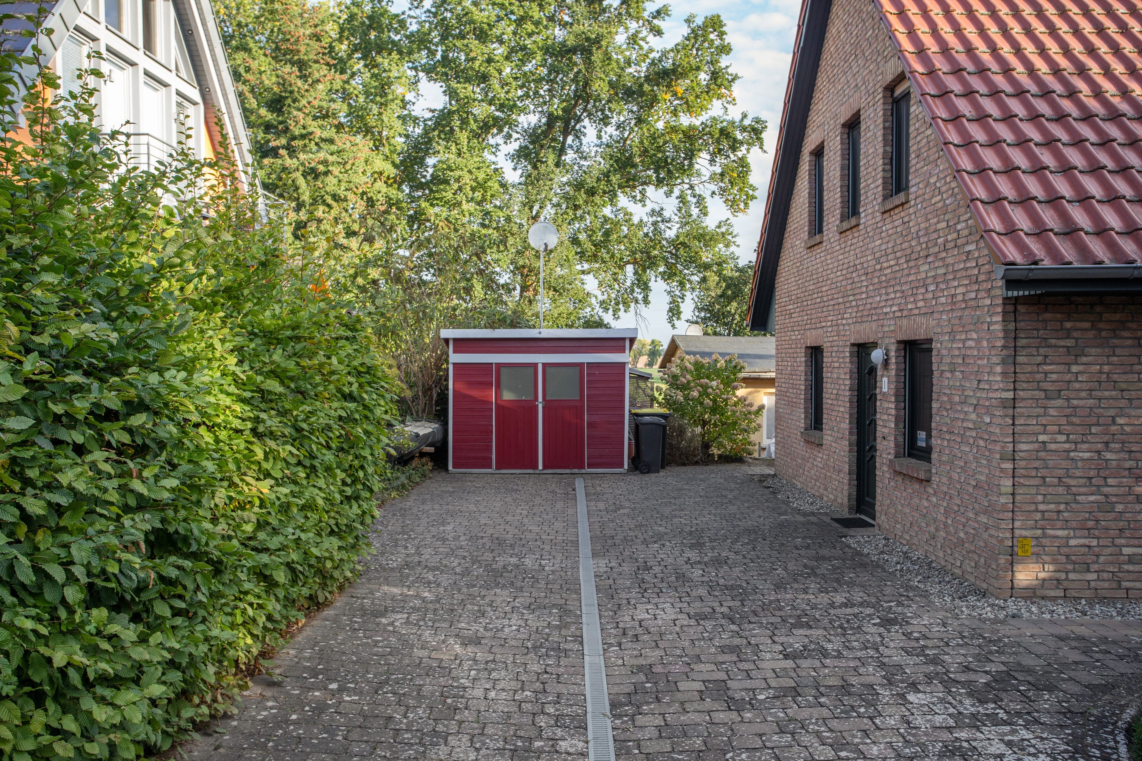A courtyard with a red shed, cobblestone path, and a brick building.