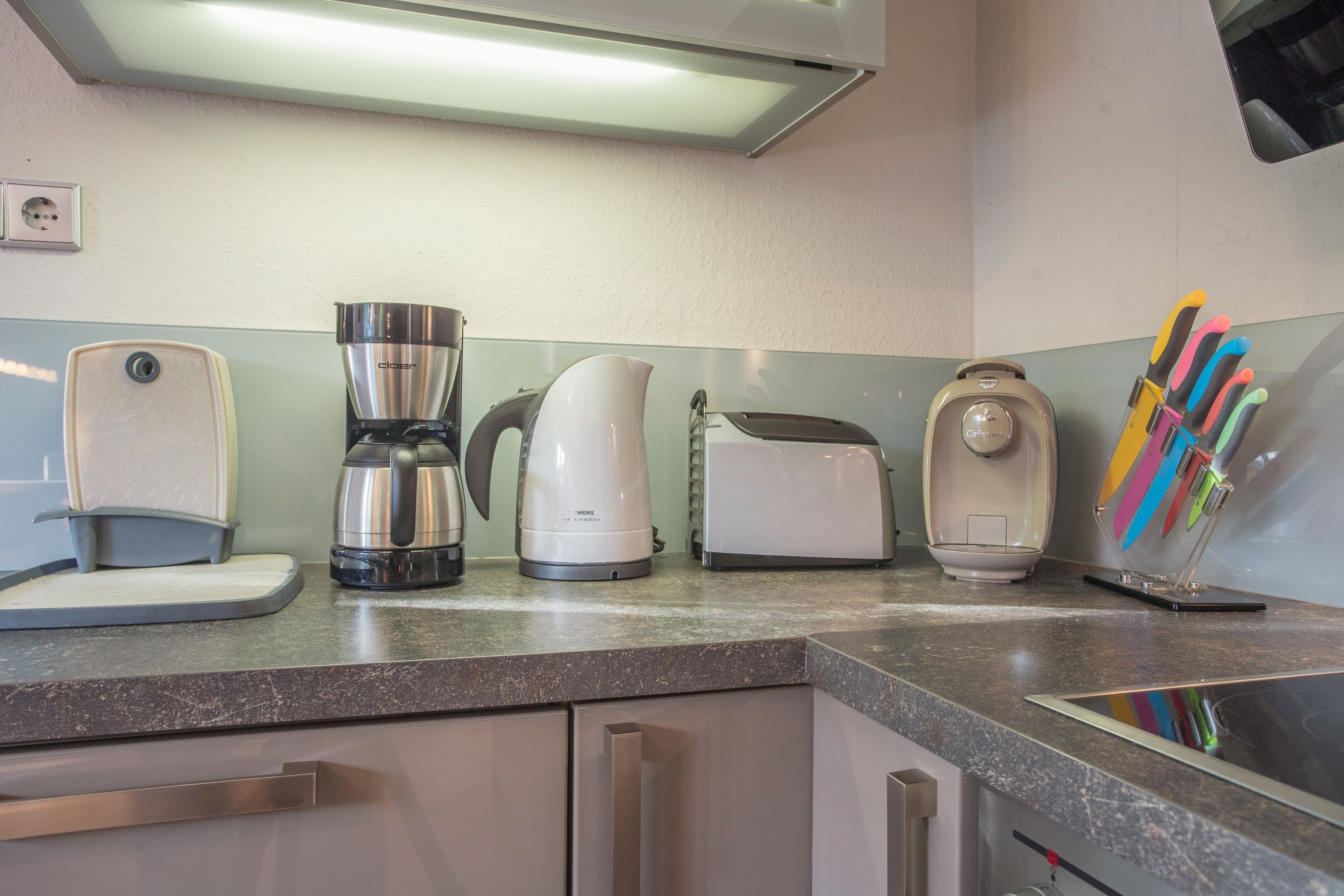 A kitchen with a coffee maker, toaster, kettle, and a knife block on the counter.