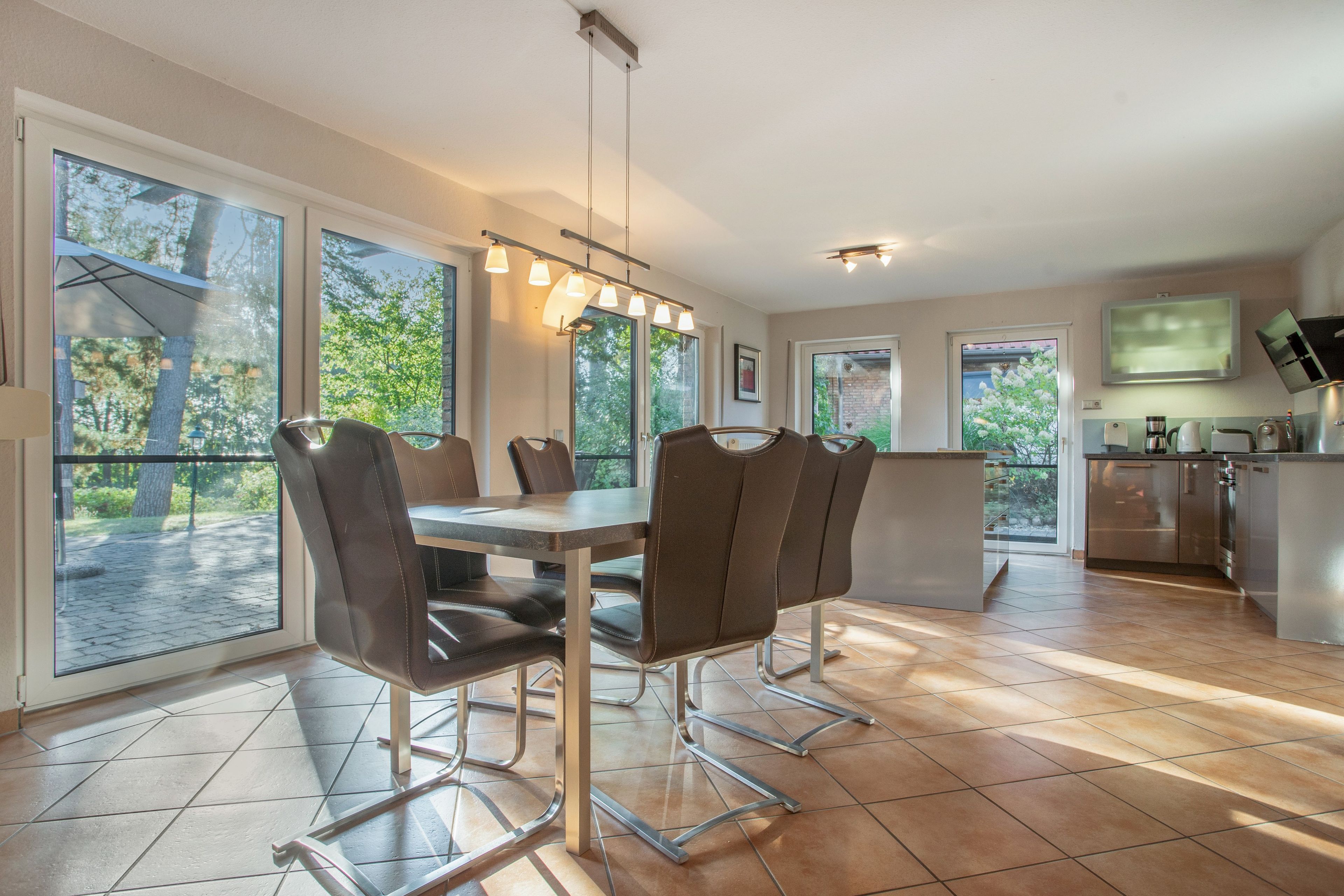 A modern kitchen with a dining area, large windows, and a view of the outdoors.