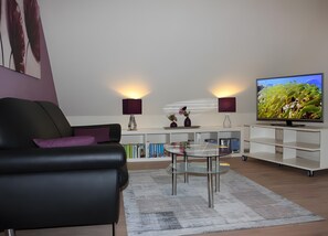 Ein modernes Wohnzimmer mit einer schwarzen Couch, einem Glastisch, einem Fernseher und einem weißen Schrank.