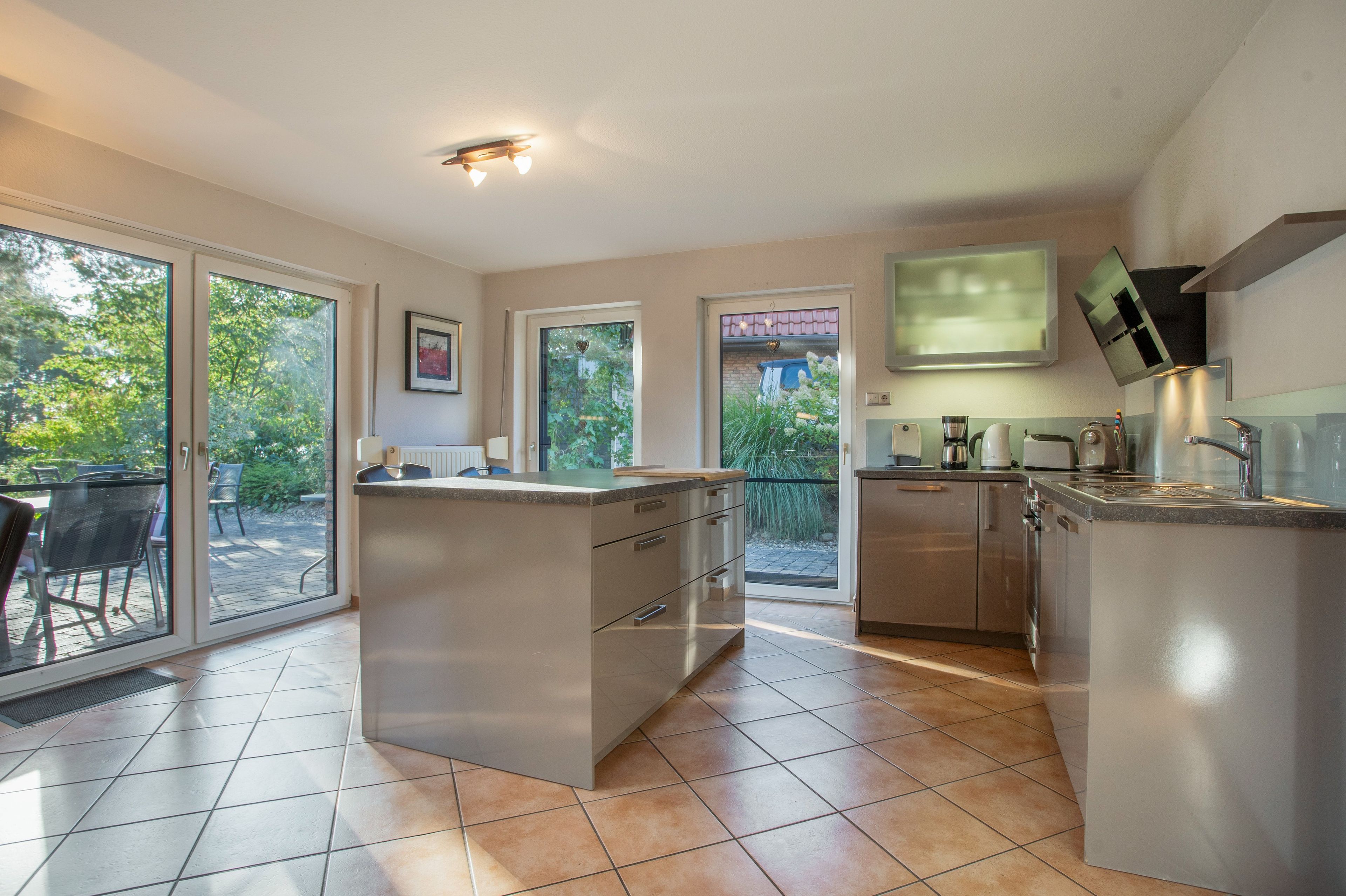 A modern kitchen with a central island, a dining area with chairs, and large sliding glass doors leading to a patio.