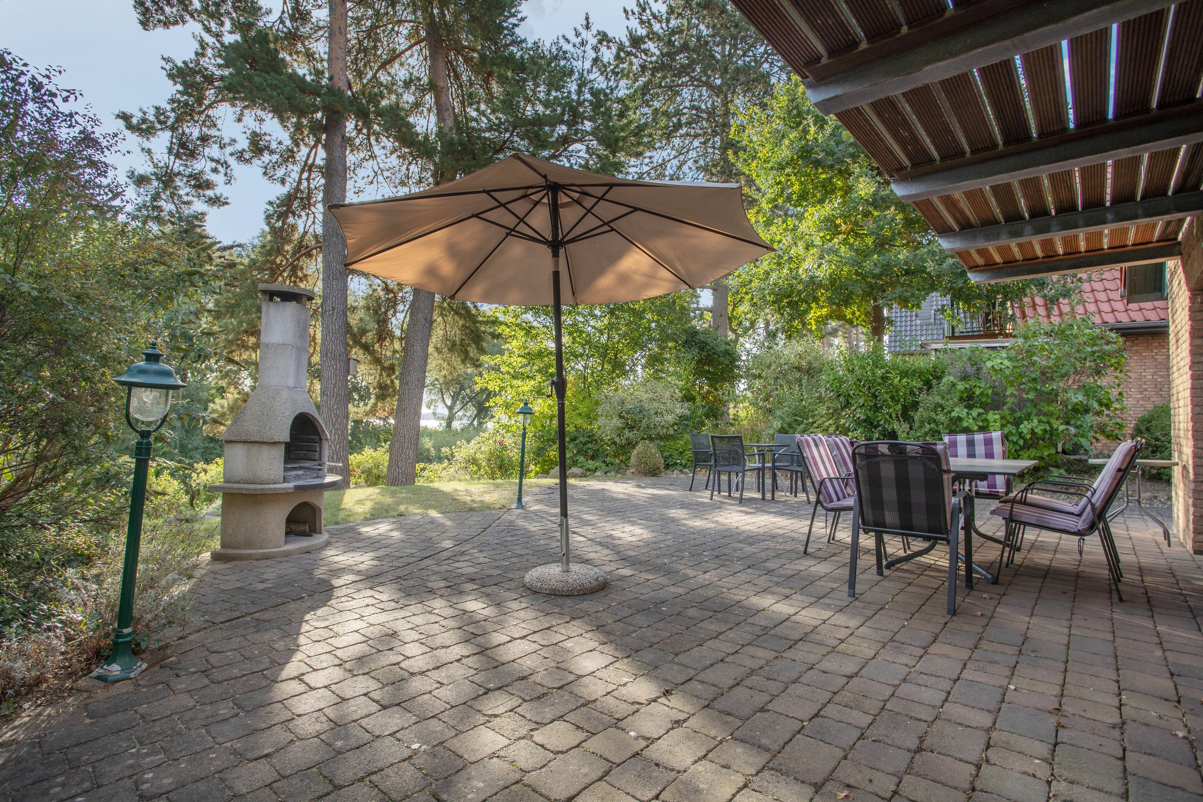 A patio with a brick floor, outdoor seating, a stone fireplace, and a pergola structure.
