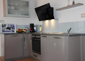 A modern kitchen with a built-in oven, a coffee maker, and a flat-screen TV mounted on the wall. - Holiday Home 'Haus 1' with Lake View, Private Terrace and Wi-Fi (Röbel)