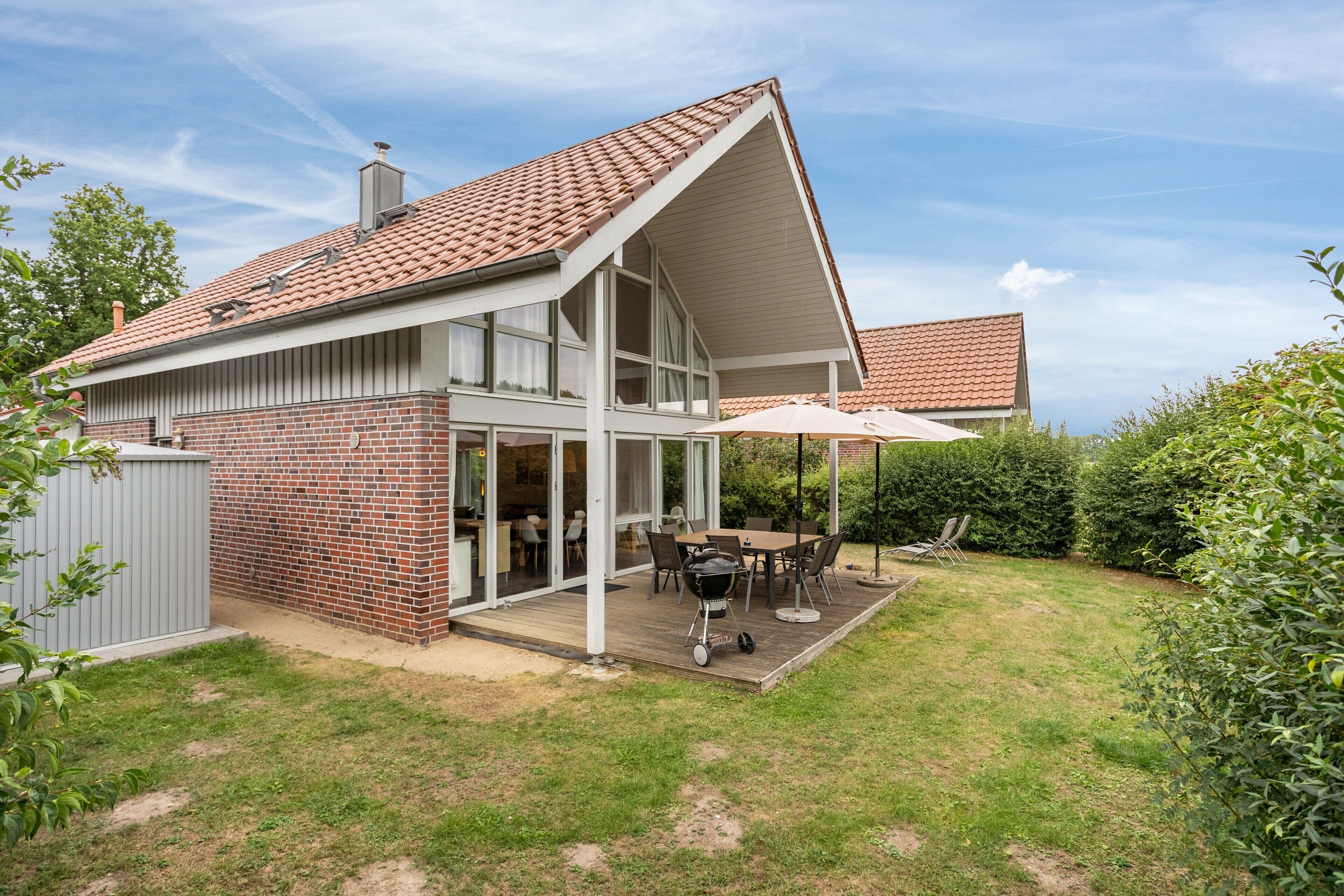 A two-story house with a brick exterior, a covered patio with a table and chairs, and a visible chimney.