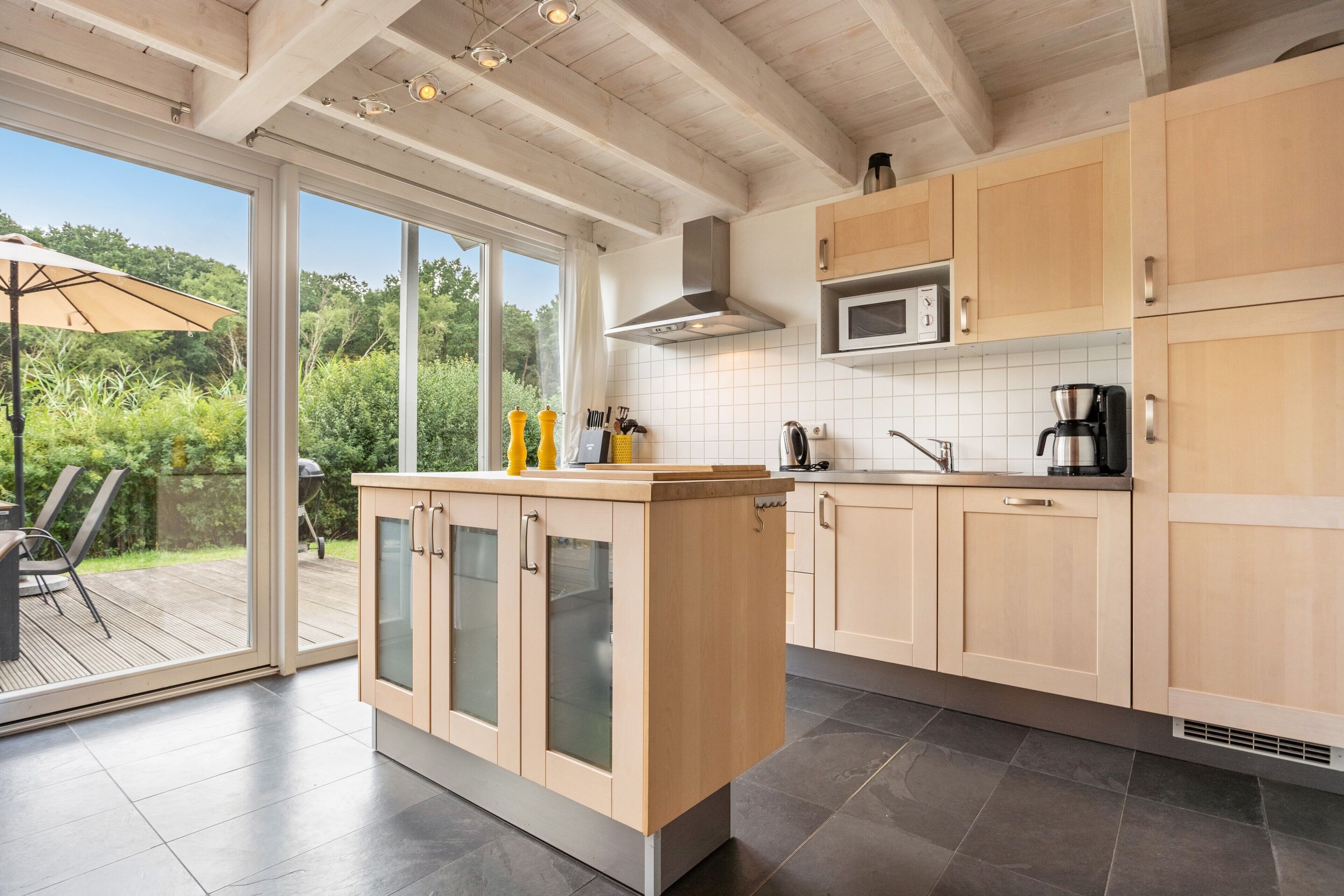 A modern kitchen with a large island, stainless steel appliances, and a view of a garden through the sliding glass doors.