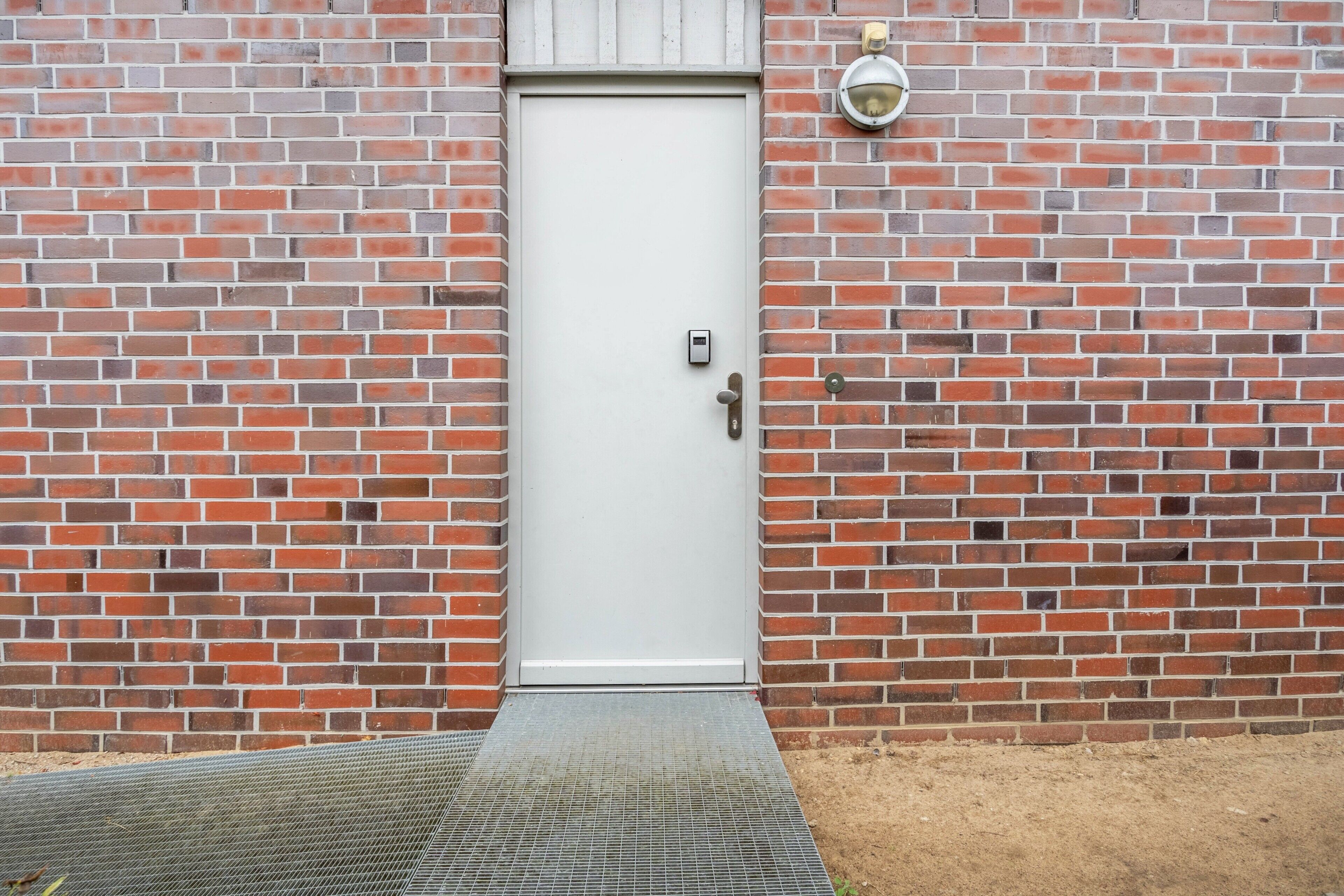 A white door with a metal handle, a small mailbox, and a metal step leading to a brick wall.