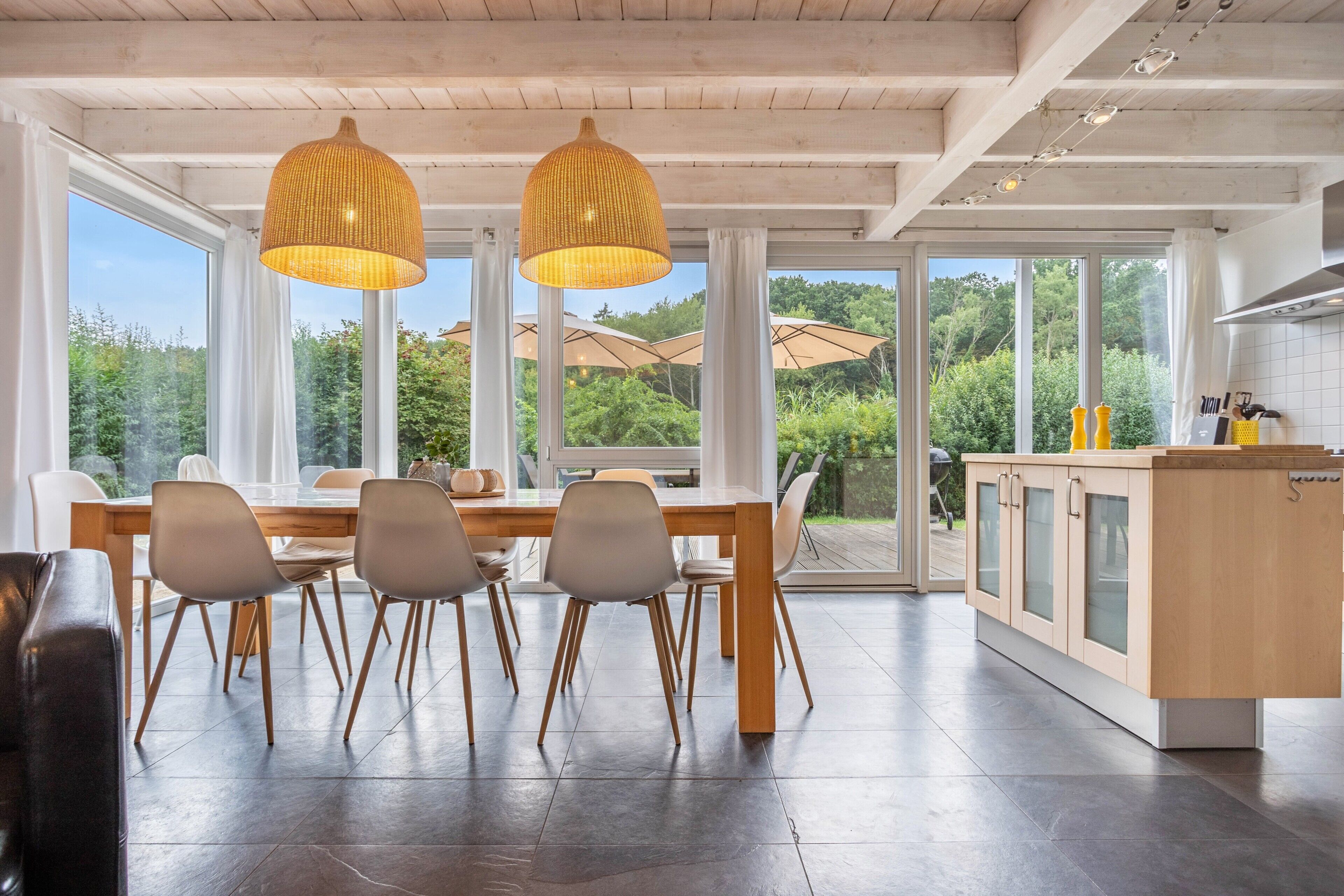 A modern kitchen with a dining area, large windows, and a view of the outdoors.
