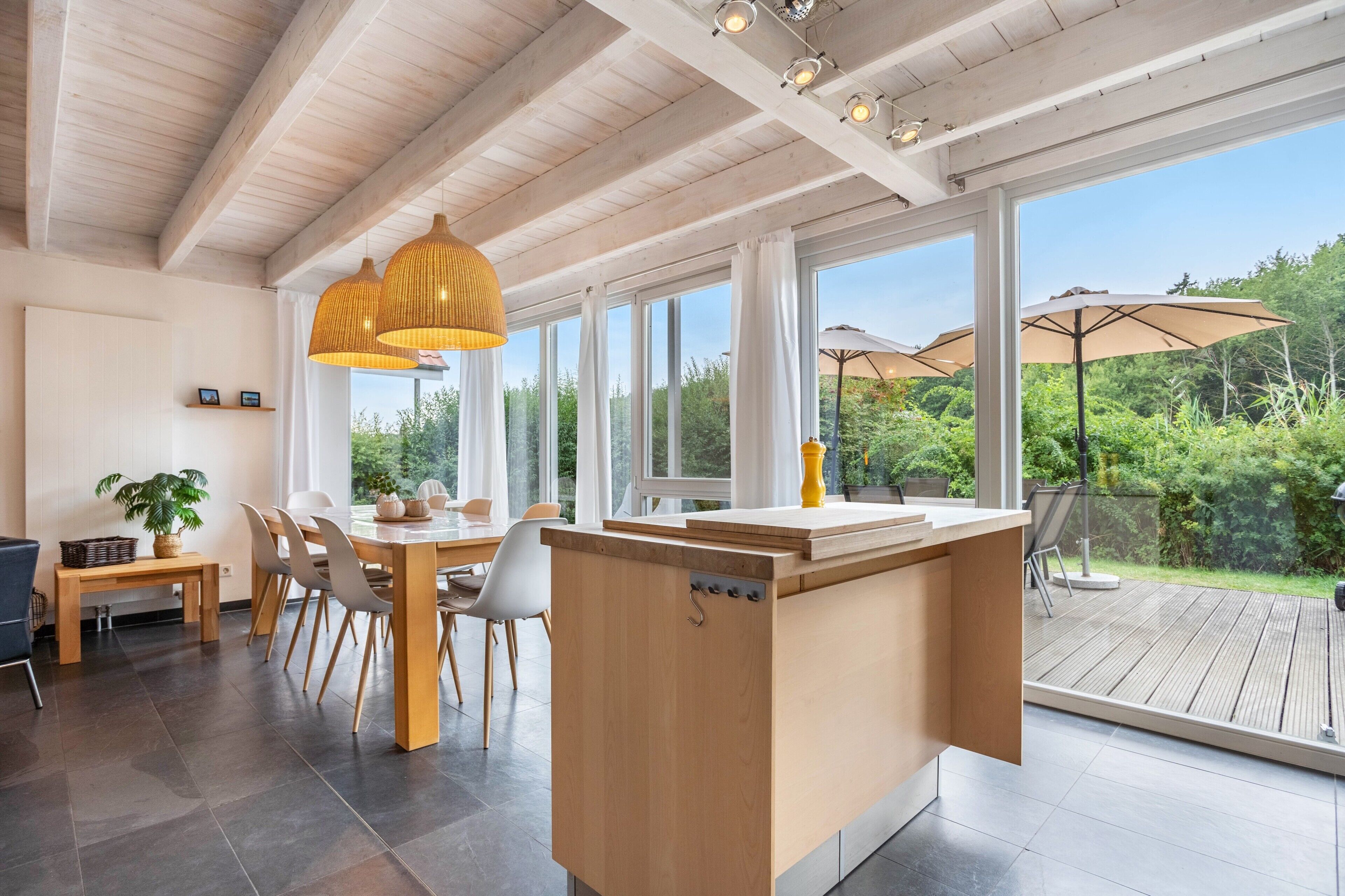 A modern kitchen with a wooden island, large windows, and a view of the outdoors.