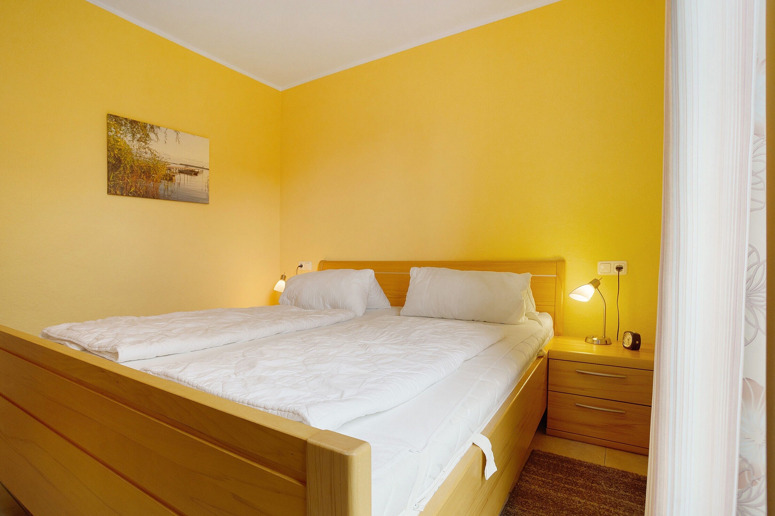 A single bed with a wooden frame, a bedside table with a lamp, and a wall-mounted picture.